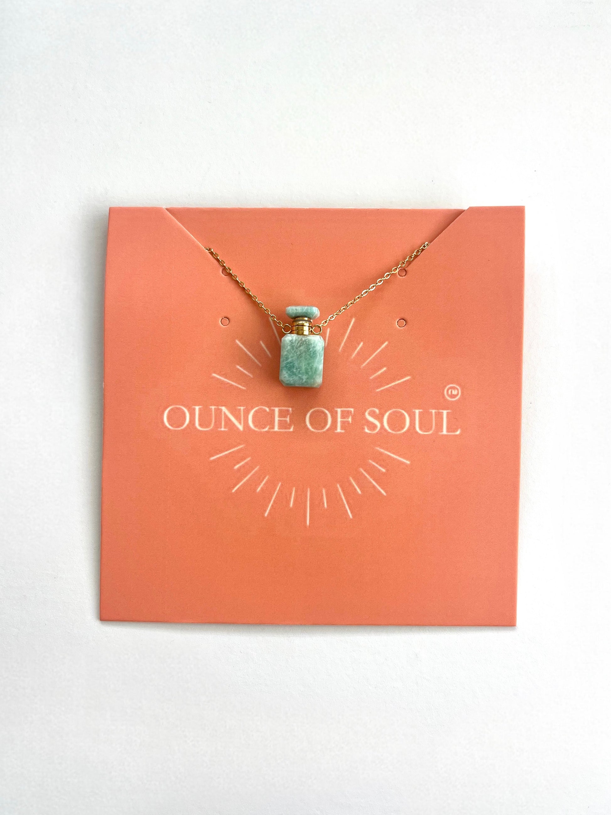 An amazonite creamation bottle necklace presented on an orange card with the text 'OUNCE OF SOUL', the necklace features a small pendant vial containing a blue substance, and an 18-inch chain.