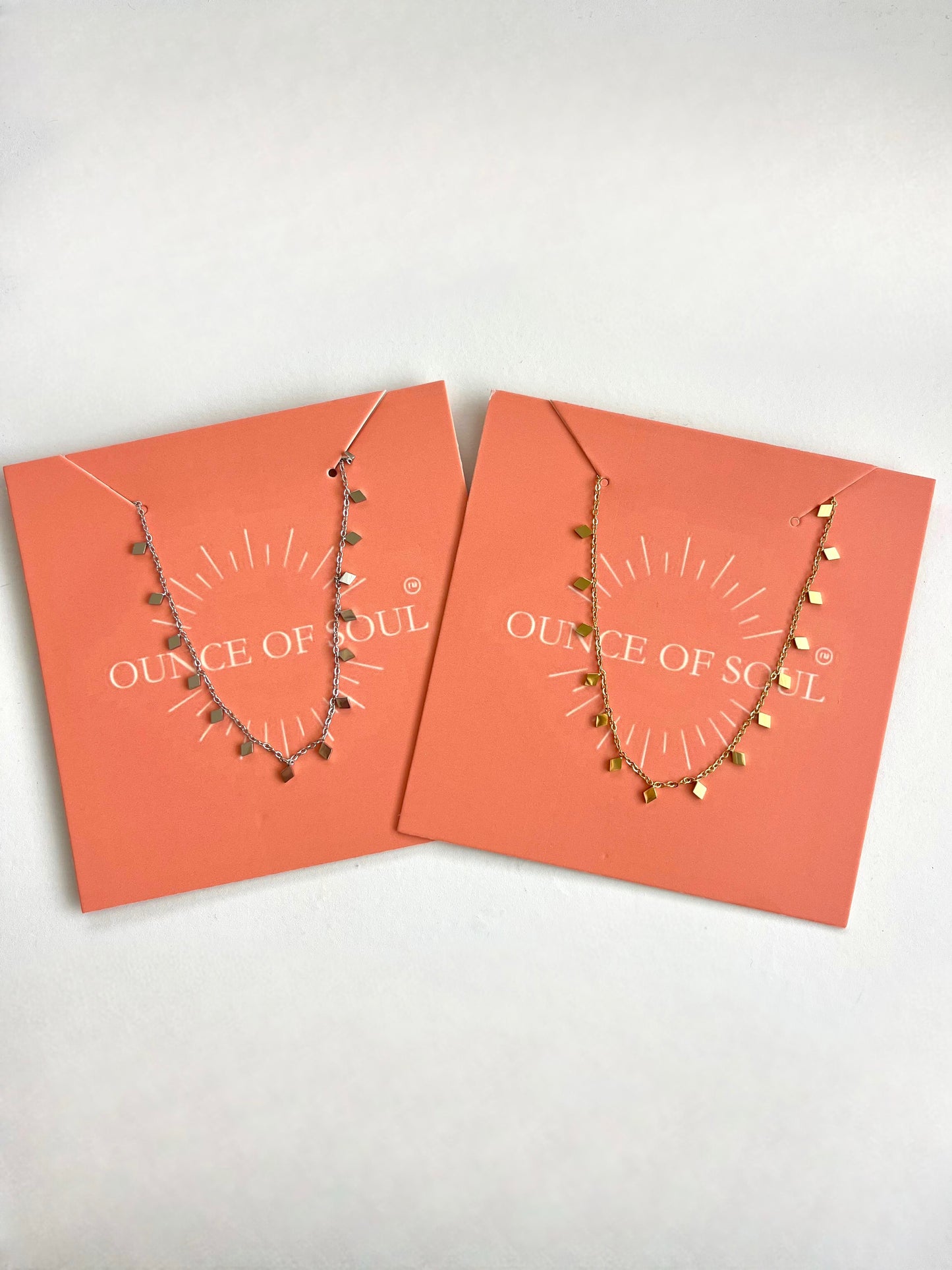 Two necklaces with diamond shape charms on orange cards with 'Ounce of Soul' branding on a white background