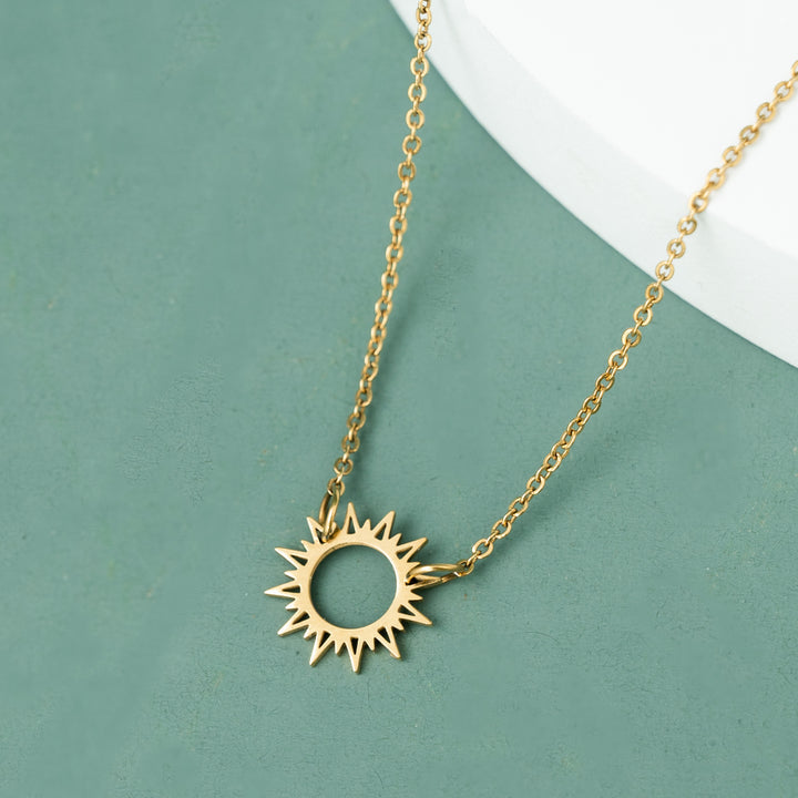 Gold sun-shaped pendant necklace on a green background